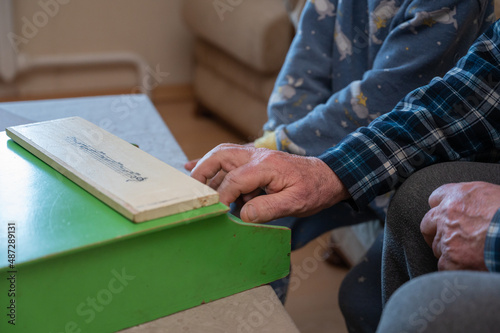 A grandfather teaches his grandson to play the toy piano. The elderly man's hands press the keys of a small children's musical instrument.