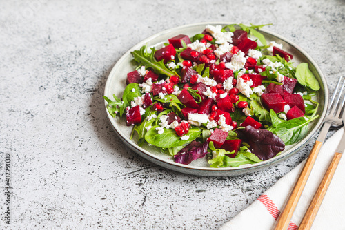 Arugula, Beet and cheese salad with pomegranate and dressing on plate on grey stone kitchen table background, place for text, top view