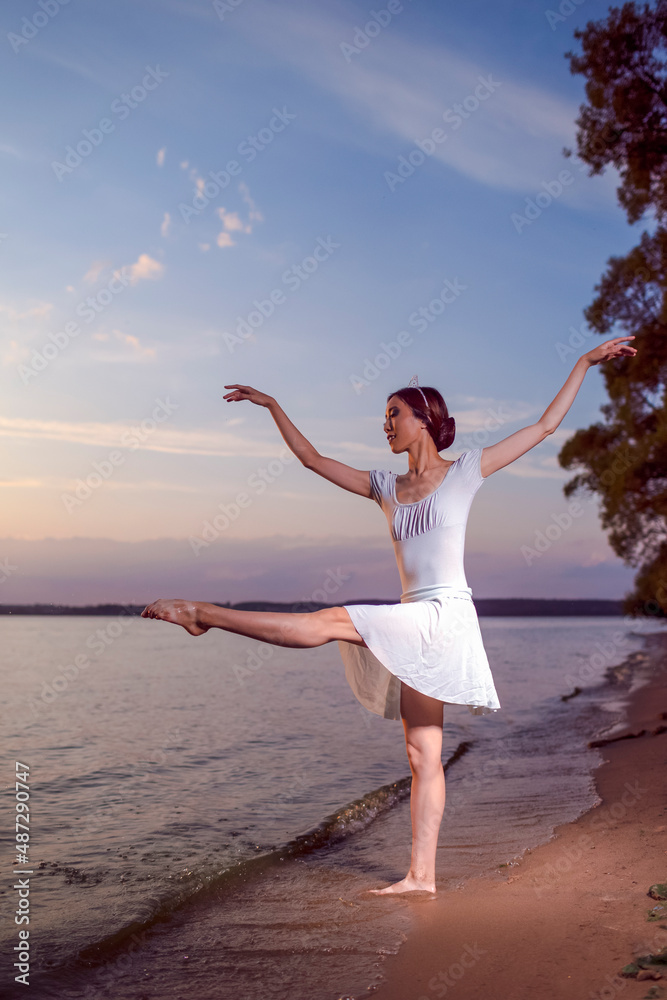 Passion To Dance With Japanese Ballet Dancer in White Dress And Silver  Crown Dancing To The Ocean Waves And Showing Ballet Pas With Lifted Hand  Against Picturesque Sunset At Sea. Stock Photo