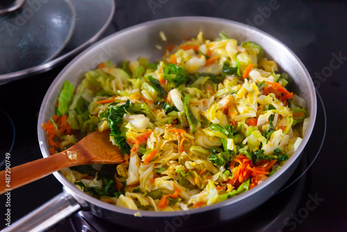 Cabbage in frying pan on electric stove, process of stewed cabbage preparation