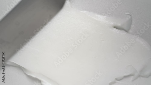 Spreading antiaging squeezed cream jet with spatula over white background upper macro view. Professional cosmetic product for beauty