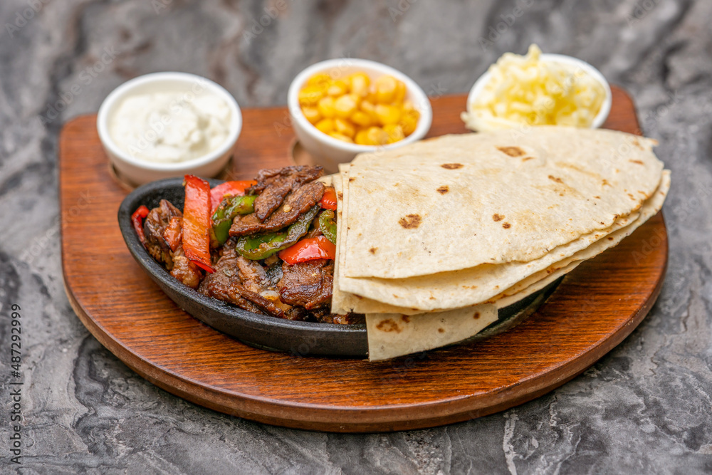 Meat fajitas on black stone plate with sauces