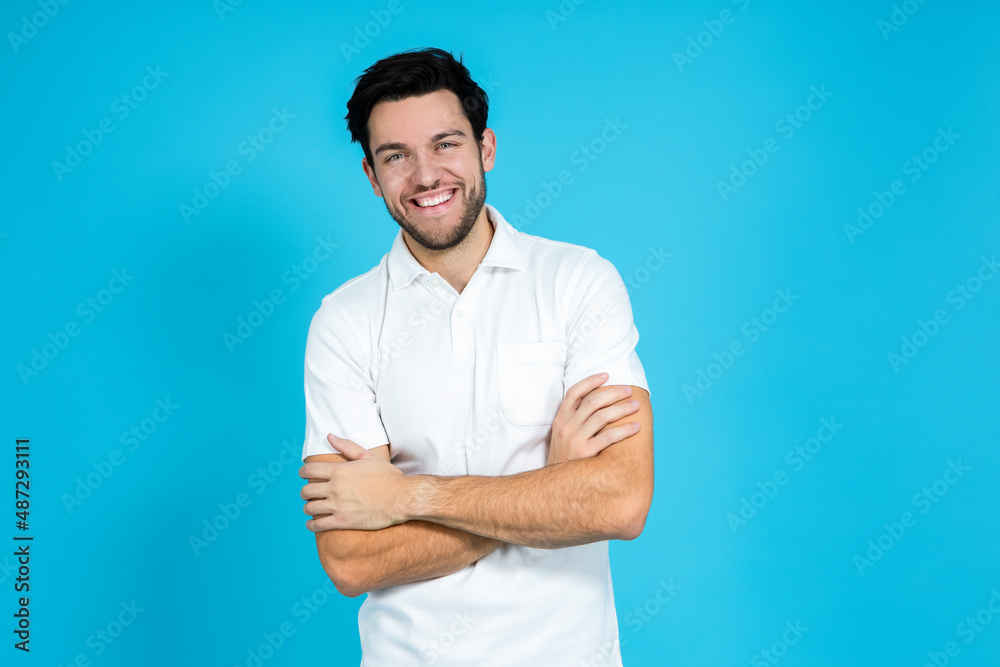 Lifestyle Ideas. Caucasian Handsome Man Posing in White Shirt Smiling Looking Straight to Camera And Holding Hands Folded Over Blue Background. Lifestyle Ideas. Caucasian Handsome Man Posing in White Shirt Smiling Looking Straight to Camera And Holding Hands Folded Over Blue Background.