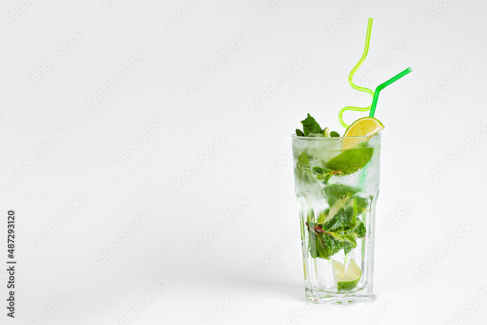 Green cocktail on a white background. Alcoholic mojito with ice close up. Lime, mint and straw in a cocktail. Copy space and wine place for text near the glass.