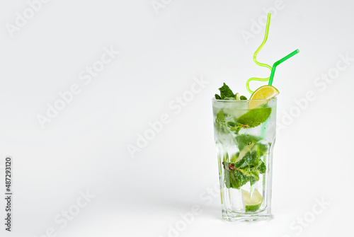 Green cocktail on a white background. Alcoholic mojito with ice close up. Lime, mint and straw in a cocktail. Copy space and wine place for text near the glass.