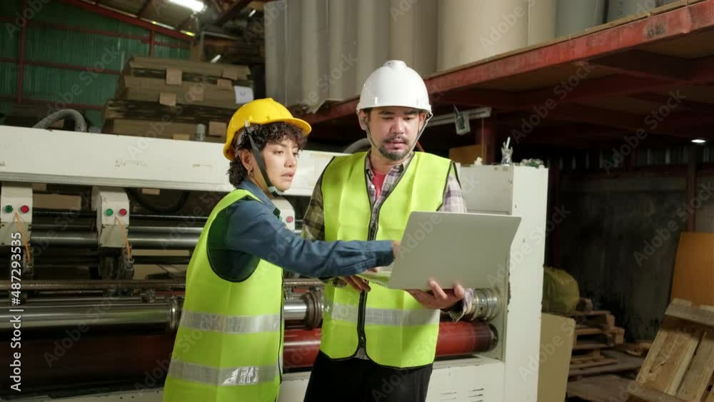 Safety uniform workers and industrial engineers with hardhat use laptop computer to check and control machines. Two professionals work in paper manufacturing factory, maintain production equipment. Safety uniform workers and industrial engineers with hardhat use laptop computer to check and control machines. Two professionals work in paper manufacturing factory, maintain production equipment.