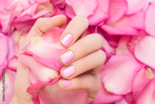 Female hand with glitter pink nail design. Female hand hold spring pink rose petals. Woman hand with pink manicure on pink petals background