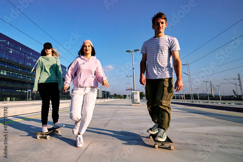 Three excited teenagers spend time in the urban exterior. They are running and skateboarding.