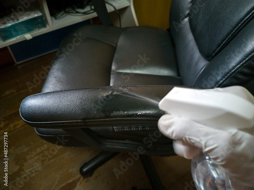 High angle view, cleaning a black work chair, using alcohol spray, spraying the armrests, white gloved hands. photo