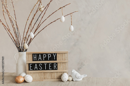Stylish box text frame with happy easter lettering. Beige, white, gold and grey eggs are under osier, pussy-willow branches. Copyspace.
