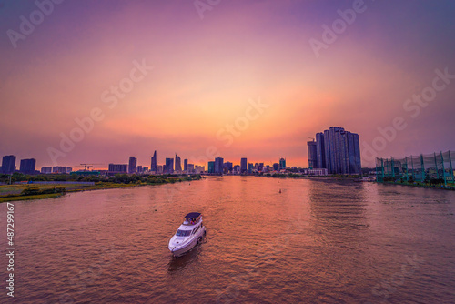 Tourist yacht on Saigon river, aerial view. Center Ho Chi Minh City, Vietnam with development buildings, transportation, energy power infrastructure. Beatiful sunset on the city.
