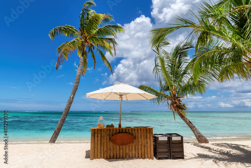 Fototapeta Naklejka Na Ścianę i Meble -  Beach cafe on sandy beach under straw umbrella, palm trees and beautiful sea on exotic tropical island.