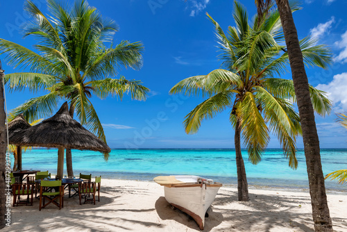 Beach cafe on sandy beach under straw umbrella, palm trees and beautiful sea on exotic tropical island. © lucky-photo