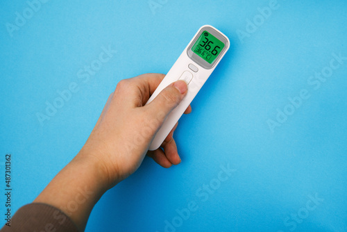 Non-contact infrared thermometer isolated on blue background. Hand holding thermometer. Anti virus protect concept. Medical office measurement product. Healthcare home action. Prevent sick procedure. 