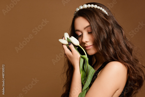 Spring lady with beautiful tulip flowers. Portrait of a young caucasian model woman with gentle makeup posing with tulip flowers over beige background
