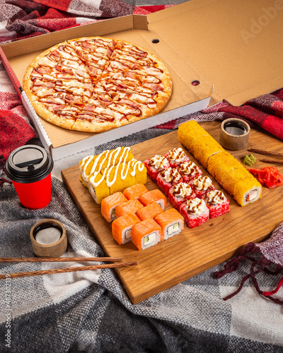 
Pizza, sushi food photo for menu. Dinner in the warmth of the house on cozy blankets. Delivery of sushi rolls and pizza during the pandemic. Combo set of rolls and pizza