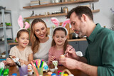 Happy caucasian family of four people decorates easter eggs at home