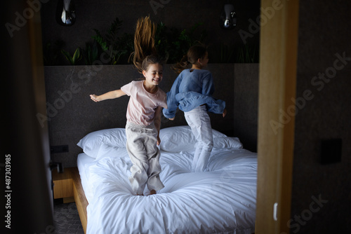 Two little sister jumping on bed indoors in hotel.