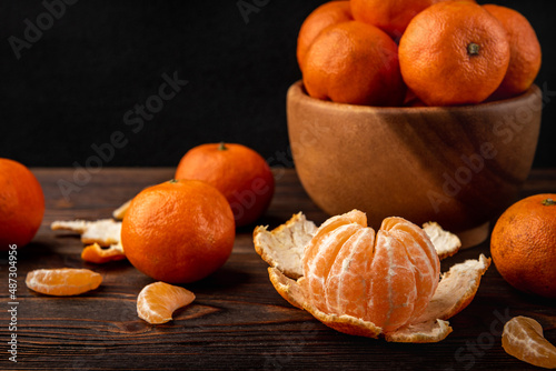 Mandarin with peeled slices on dark wooden background.