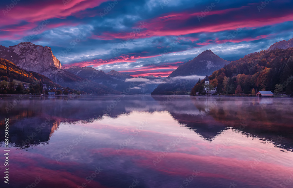 Sunrise view on Alps above Grundlsee lake. Colorful cloudy sunset over the hills with Alpine lake. Amazing nature scenery with reflection in the calm water. Grundlsee. Austria. Europe