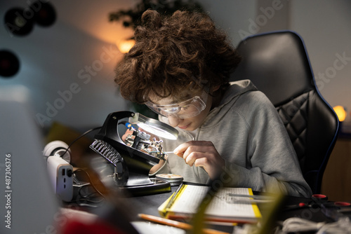 Bilde på lerret Afro boy wearing safety glasses soldering motherboard in room at desk