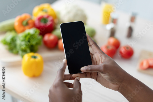 Hands of young african american woman hold smartphone with blank screen making photo on table