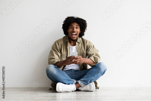Online Sale. Excited happy black guy holding smartphone and looking at camera