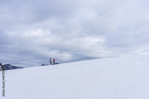 two people on cross country ski moving on a hill full of snow on the horizon with cloudy sky
