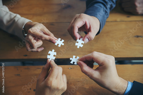 Strategy and Solution Business Concept. Group of Business people holding piece of jigsaw puzzle to solution problem on wooden desk, Collaborate between Professional Businessman and Partnership
