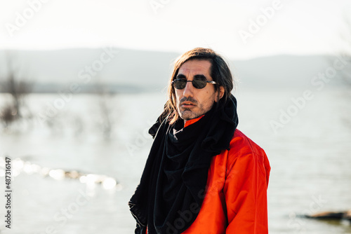 man with sunglasses looking at the camera in front of the sea on a cold day © 23_stockphotography