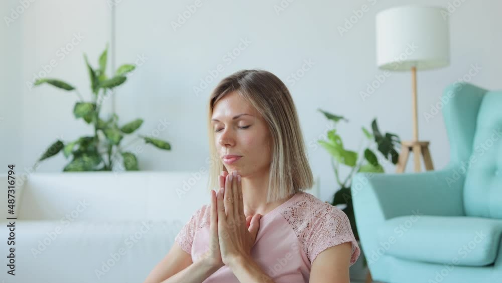 Young woman meditating and practicing yoga while sitting on floor in home room spbi. 4k video Beautiful caucasian female does asana with smile and joins hands in mudra, meditates and sits on mat in Young woman meditating and practicing yoga while sitting on floor in home room spbi. 4k video Beautiful caucasian female does asana with smile and joins hands in mudra, meditates and sits on mat in