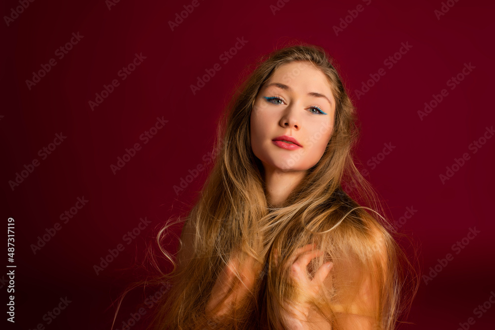 Beautiful model girl with long blond hair. Red background. Care and beauty hair products. Fashion, cosmetics and makeup.