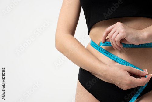 Young slim woman in a black top and panties measures her body with a blue measuring tape. Healthy food and diet concept.