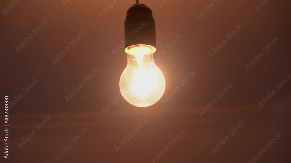 A lamp with a tungsten bulb assembly slowly turns on and off on a black background, a close-up shot of an old retro-vintage light bulb brightening the light. A comfortable cozy concept.
