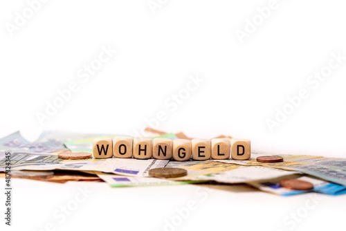 German word for housing allowance, WOHNGELD, spelled with wooden letters wooden cube on a plain white background with banknotes and coins, concept image