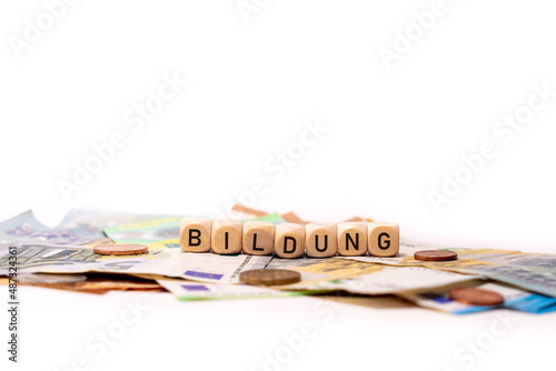German word for education, BILDUNG, spelled with wooden letters wooden cube on a plain white background with banknotes and coins, concept image