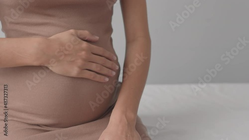 Midsection slowmo shot of female doctor examining tummy of unrecognizable pregnant woman in tight beige dress, sitting on examination couch during appointment photo