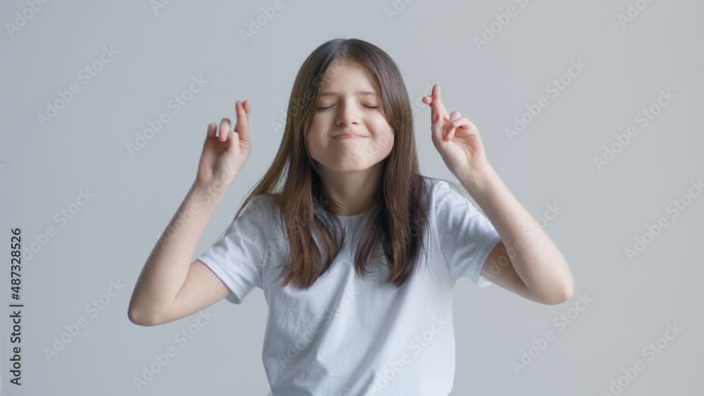A blonde teenager girl in a white T-shirt holds her fingers cross on the background of a white wall A blonde teenager girl in a white T-shirt holds her fingers cross on the background of a white wall
