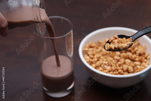 Chocolate milk is pouring into a glass. Ready cereal in a white cup. photo