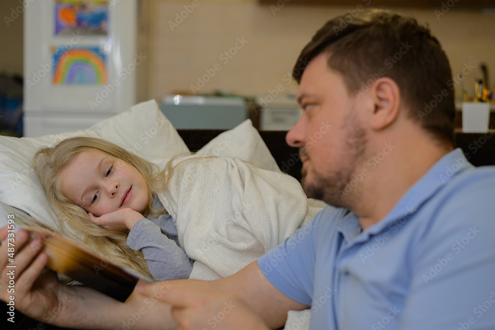 dad entertains the child during illness: he looks, reads a book, a photo book with his daughter home. The father suspects that his daughter is ill. The child is not feeling well. the concept of