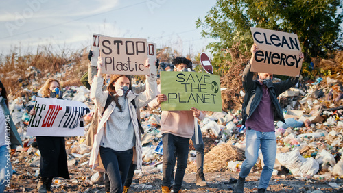 Young Generation Care About the Future. Group of Young Volunteers in Gas Masks With a Poster Calling to Take Care of the Environment While Going Trough at Garbage Dump.