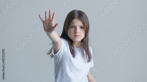 Blonde teenager girl in a white T-shirt angrily raises her hand stop against the background of a white wall