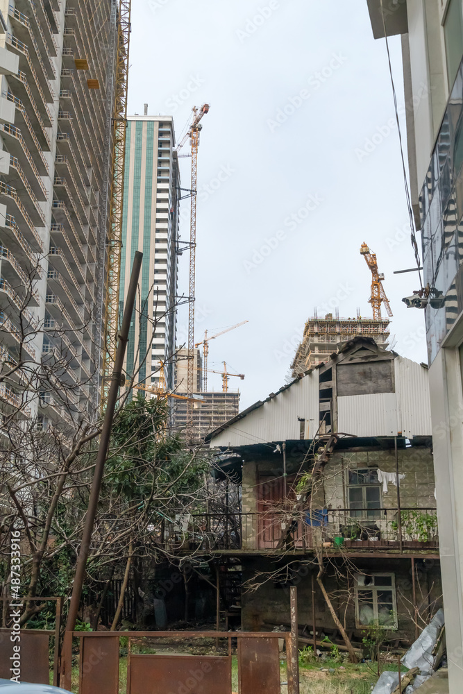 Old dilapidated brick house stands against the background of new high-rise city houses under construction. Concept of urbanization. Vertical photo Old dilapidated brick house stands against the background of new high-rise city houses under construction. Concept of urbanization. Vertical photo