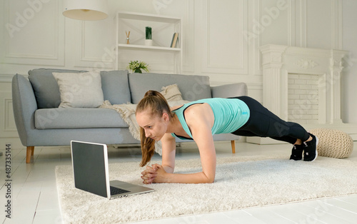 Young Woman Exercising at Home Online Via Laptop During Quarantine. The Girl Does the Bar During Fitness Workout, She Leads a Healthy Lifestyle.