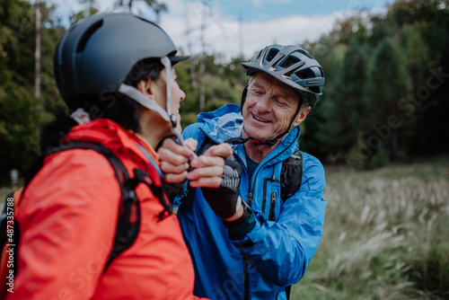 Senior couple bikers putting on cycling helmet outdoors in forest in autumn day.