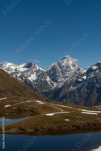 Incredibly beautiful mountain landscape: green hills against the background of snowy rocky peaks. Clear blue sunny sky. Trekking to the Koruldi Lakes in Georgia