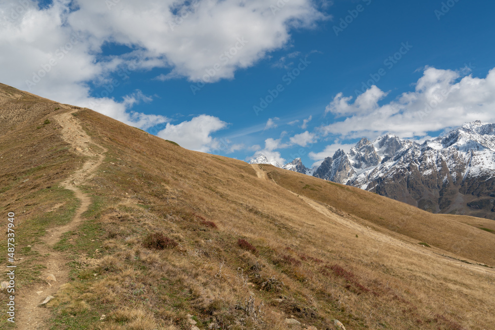 Incredibly beautiful mountain landscape: green hills against the background of snowy rocky peaks. Clear blue sunny sky. Trekking to the Koruldi Lakes in Georgia Incredibly beautiful mountain landscape: green hills against the background of snowy rocky peaks. Clear blue sunny sky. Trekking to the Koruldi Lakes in Georgia