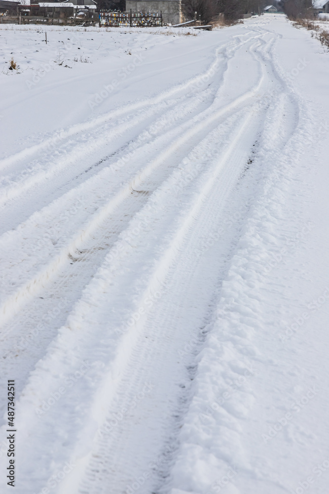 Snowy road in a field leading to pine forest. Winter road to nowhere in sunny day, snow-covered fresh car track. Car traces in a deep snow of remote rural area
