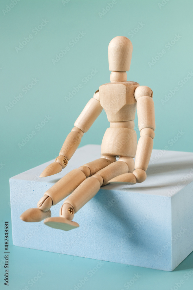 A mannequin of a man made of wood sitting on a blue podium in close-up. A mannequin of a man made of wood sitting on a blue podium in close-up.