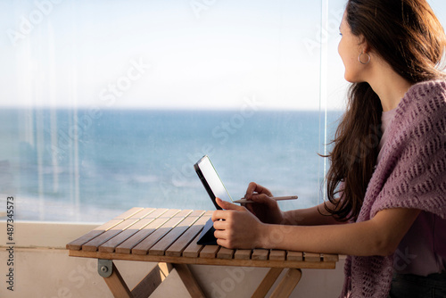 A woman is working on digital tablet on the terrace and looking at the sea